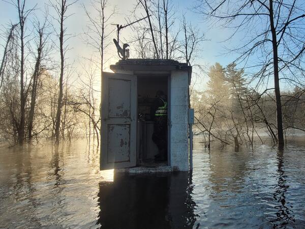Hydrologic technician servicing a flooded streamgage housing, backlit by sunrise