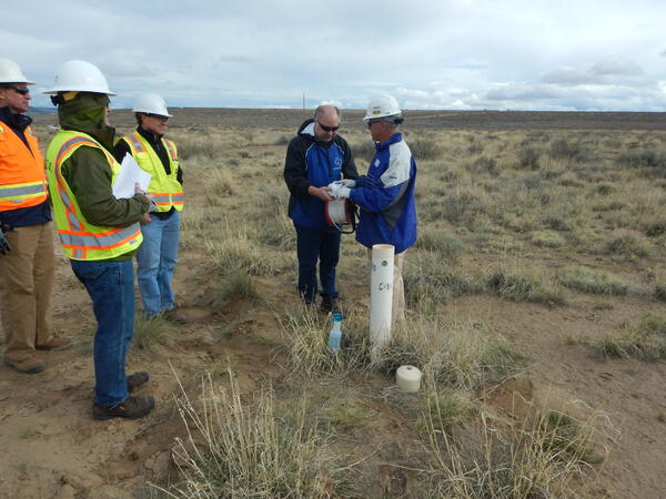 Three people in hard hats on the left hand side standing in a meadow with two men in blue jackets holding a wrapped wire.