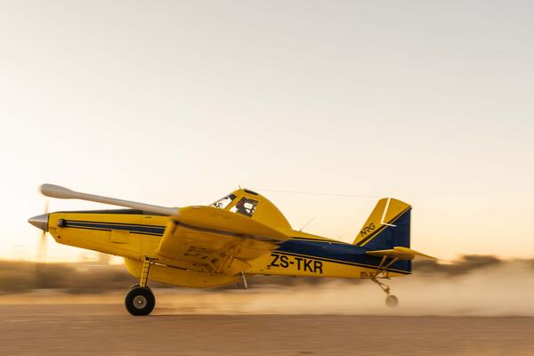 A yellow and dark blue single-engine agricultural aircraft (registration ZS-TKR)
