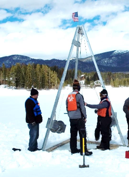 scientists in winter clothes and safety gear examine a percussion piston coring system situated on a frozen lake