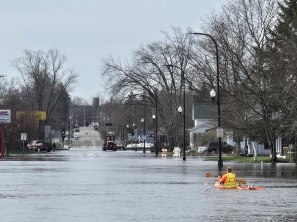 Hydrologic technician kayaks down a flooded street towing an ADCP