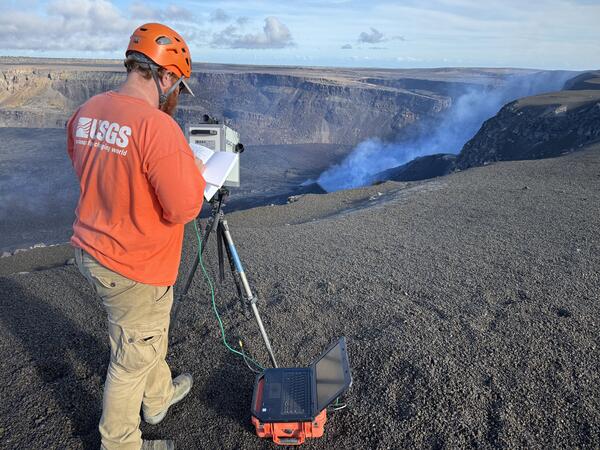 Color photograph of scientist measuring volcanic plume from crater rim