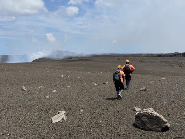 Color photograph of two scientists walking on volcanic landscape