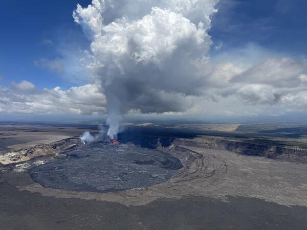 A large white and blue plume rises from the red lava fountains within a crater