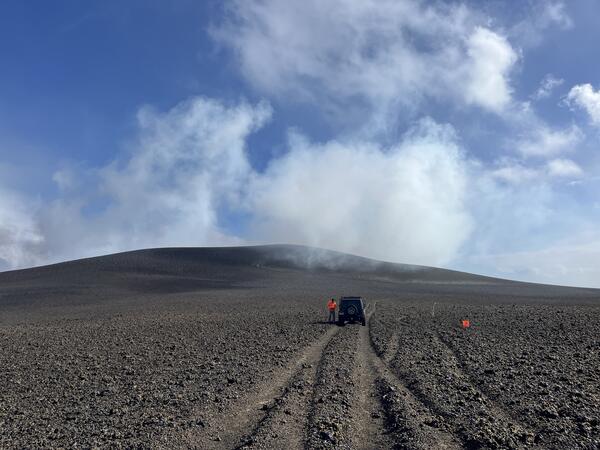 Color photograph of volcanic hill with road and vehicle in the foreground