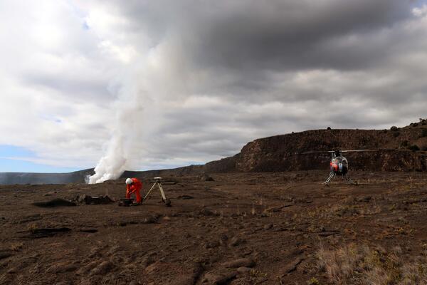 Color photograph of scientist collecting data from a monitoring station on the floor of a caldera