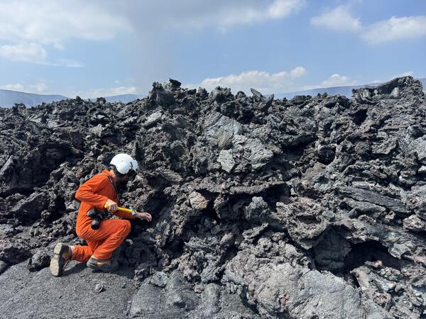 Color photograph of scientist collecting sample of lava flow