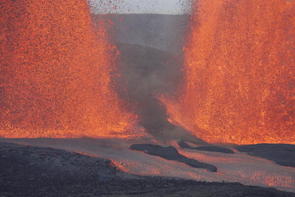 Color photograph of the base of two lava fountains and lava flowing away from them