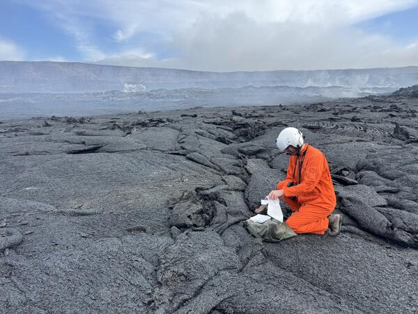 Color photograph of scientist collecting a sample from a recent lava flow