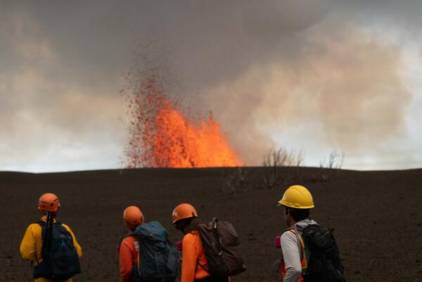 Color photograph of scientists with top of lava fountain in distance