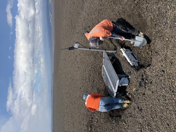 Color photograph of scientists fixing volcano monitoring equipment
