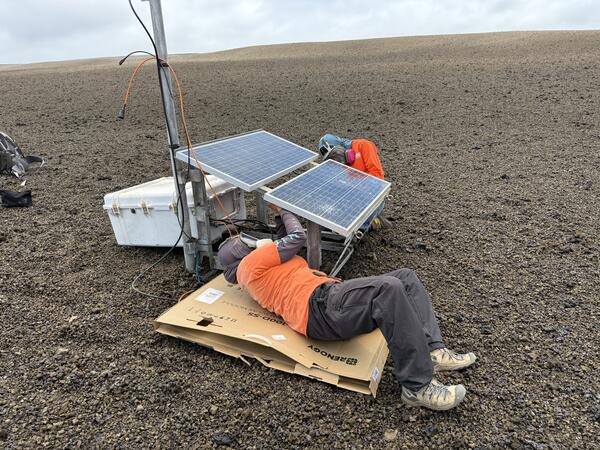 Color photograph of scientists fixing volcano monitoring station