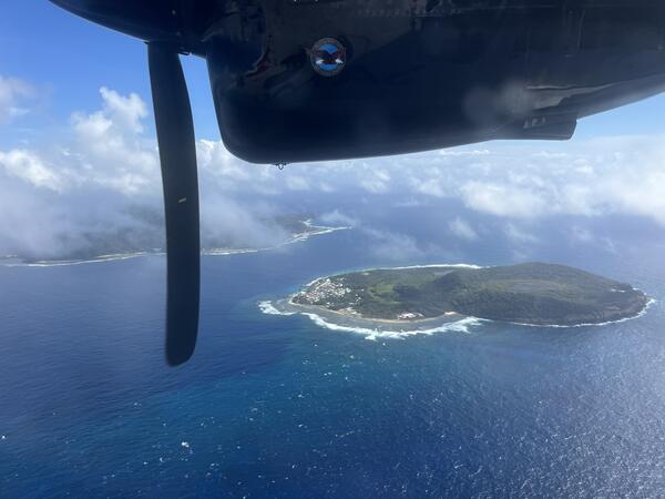 Color photograph of island with part of airplane visible in top of photo