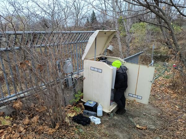 Person in bright yellow hat working on streamgage housing