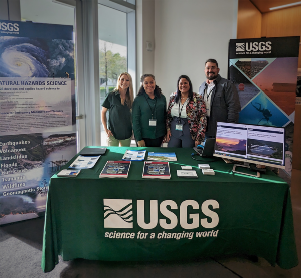 four people stand at a table draped in a green USGS tablecloth with several resources on display