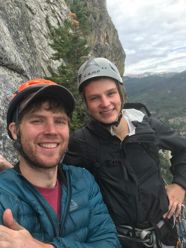 two people with climbing helmets next to vertical rock face