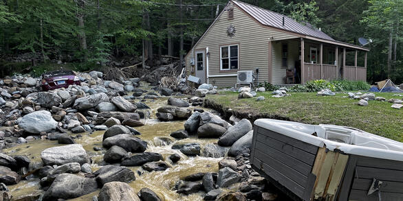 A car is covered in boulders next to a flooded yard with a displaced hot tub