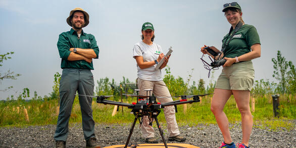 Three people standing behind a drone