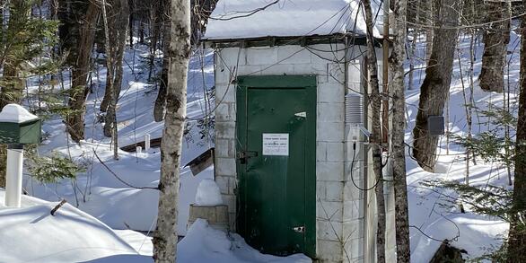 A streamgage house in a snowy, forested landscape.