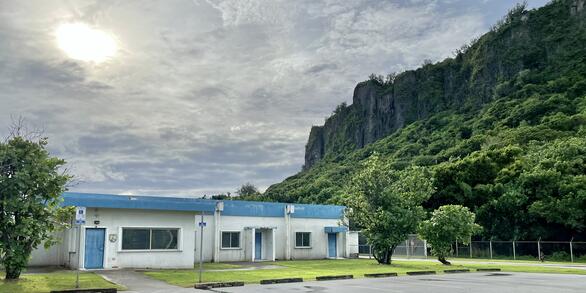 White and blue one-story building with tropical trees and cliffs