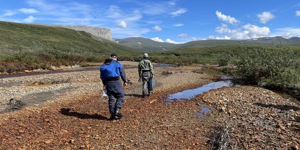 Two people walking up an orange creek bed.