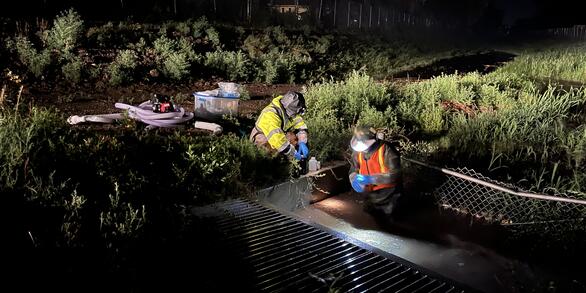 Two USGS employees sampling surface water in the dark during a rainstorm. 