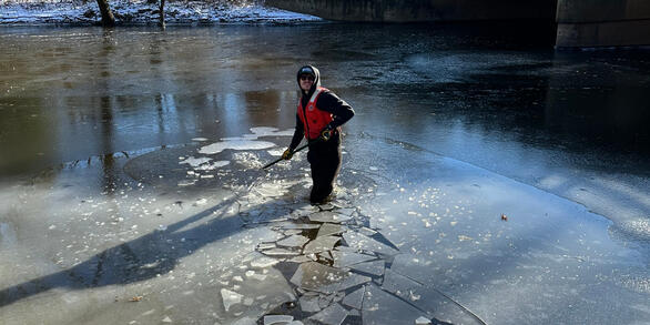Scientist breaking up and wading through ice covered river