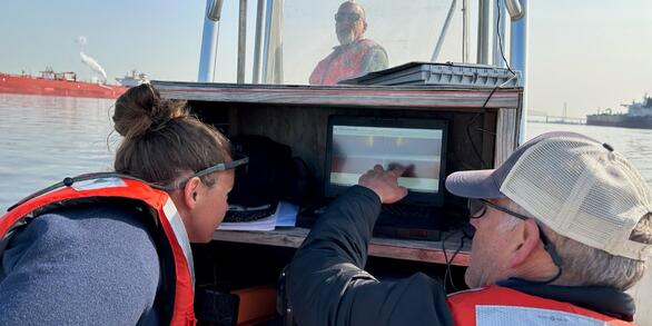 Two scientists consult a screen on a boat while looking for Atlantic sturgeon.