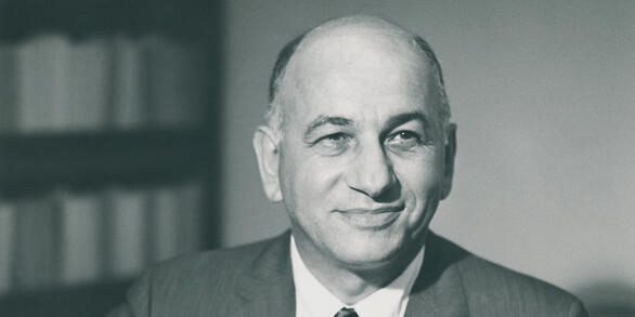 Posed portrait of William T. Pecora writing at a desk while smiling