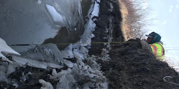 USGS hydrographer Chris Broz gets on the cold ground to measure the high-water mark of the Pembina River at Neche, North Dakota.