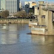 Looking across a wide city river. Wooden bridge dolphins on a concrete bridge in the main channel. tall buildings in distance