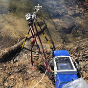 a small machine mounted to a tripod on the shore of a shallow stream 