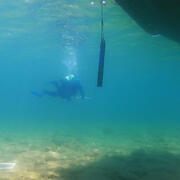 A diver approaching a scientific instrument hanging in the water beneath research vessel