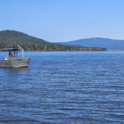 aluminum boat with a black USGS logo on vast blue lake waters. green forested hill in the background