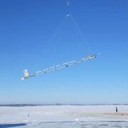 Helicopter towing large hoop over snow covered ground, technician for scale