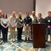 Eleven people at a conference standing in a line smiling for the camera