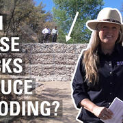 Text: Can these rocks reduce flooding? with an image of Laura Norman and a two men standing on a gabion in the background.