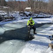 Person standing in middle of partially frozen creek with tool in the water taking measurements