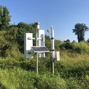 CRNS monitoring station on a grassy hillside with open blue sky overhead.