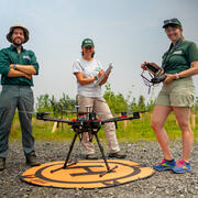 Three people standing behind a drone