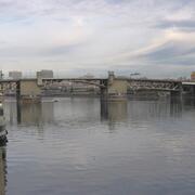 Metal and concrete bridge spans the river. Two concrete bridge piers are protected by wooden structures.
