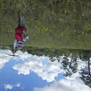 a person with red backpack and purple hat holds up a tracking device in a field with yellow flowers, trees in background