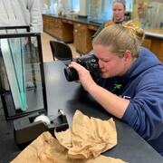 graduate student with a blonde ponytail and blue sweatshirt photographs a rosyside dace fish in a lab