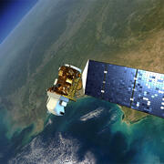 A white and gold satellite with blue solar panel attached orbits above the Earth
