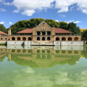 The Spanish Revival style Washington Park Lakehouse is reflected in murky green lake waters on a mostly sunny day