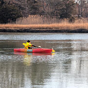 A man in a neon yellow jacket on an orange kayak in a river holding a paddle.