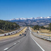 a four six lane road with frontage lanes with dozens of cars leading into snow-capped mountains