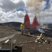Two lava fountains erupt from vents on crater floor as scientist monitors in the foreground