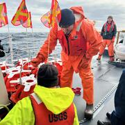 Three people on ship in the ocean, working on equipment