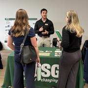 Man standing behind USGS table speaking to two women at a career fair